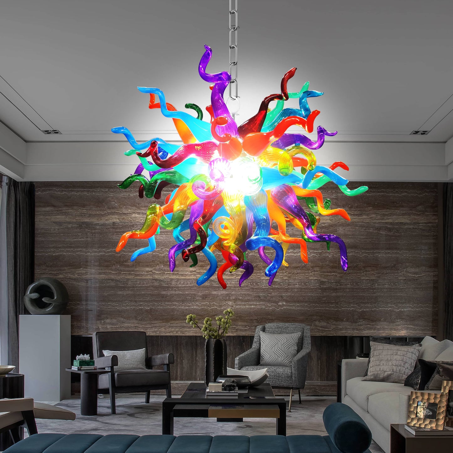 Colorful Chihuly blown glass chandelier hanging in a modern living room with gray furniture and wooden wall.