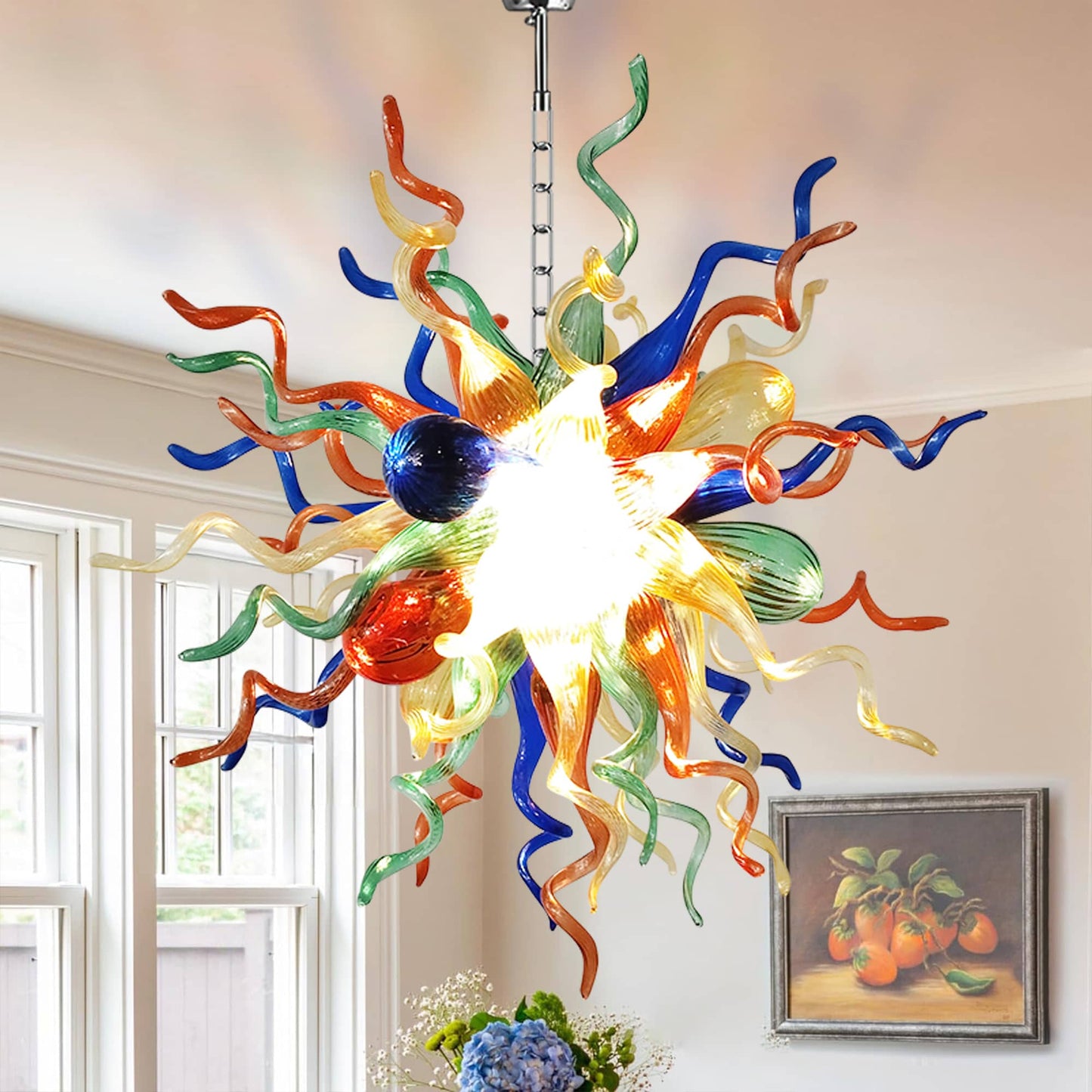 Artistic colorful blown glass chandelier illuminating a bright room, complementing a framed still-life painting.