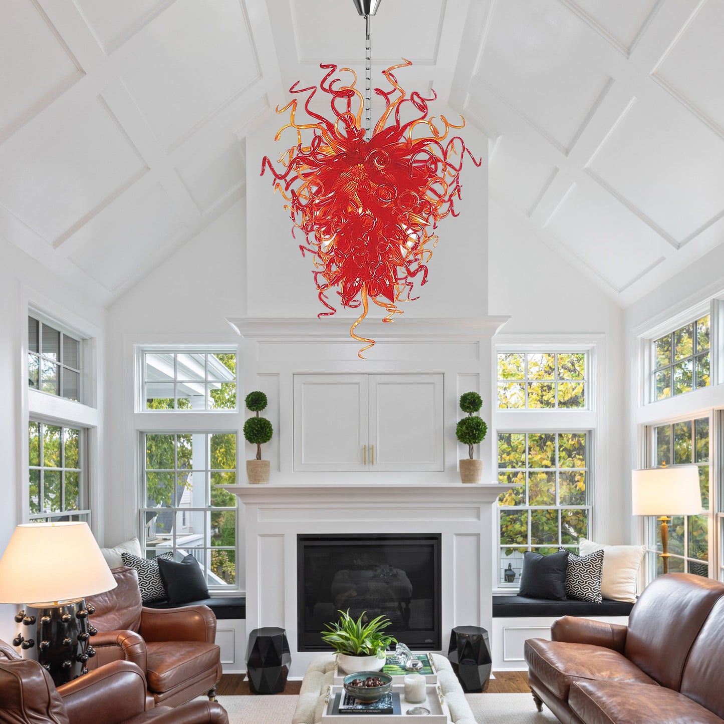 Red sculptural hand blown glass chandelier centered above a white fireplace in a modern white living room.
