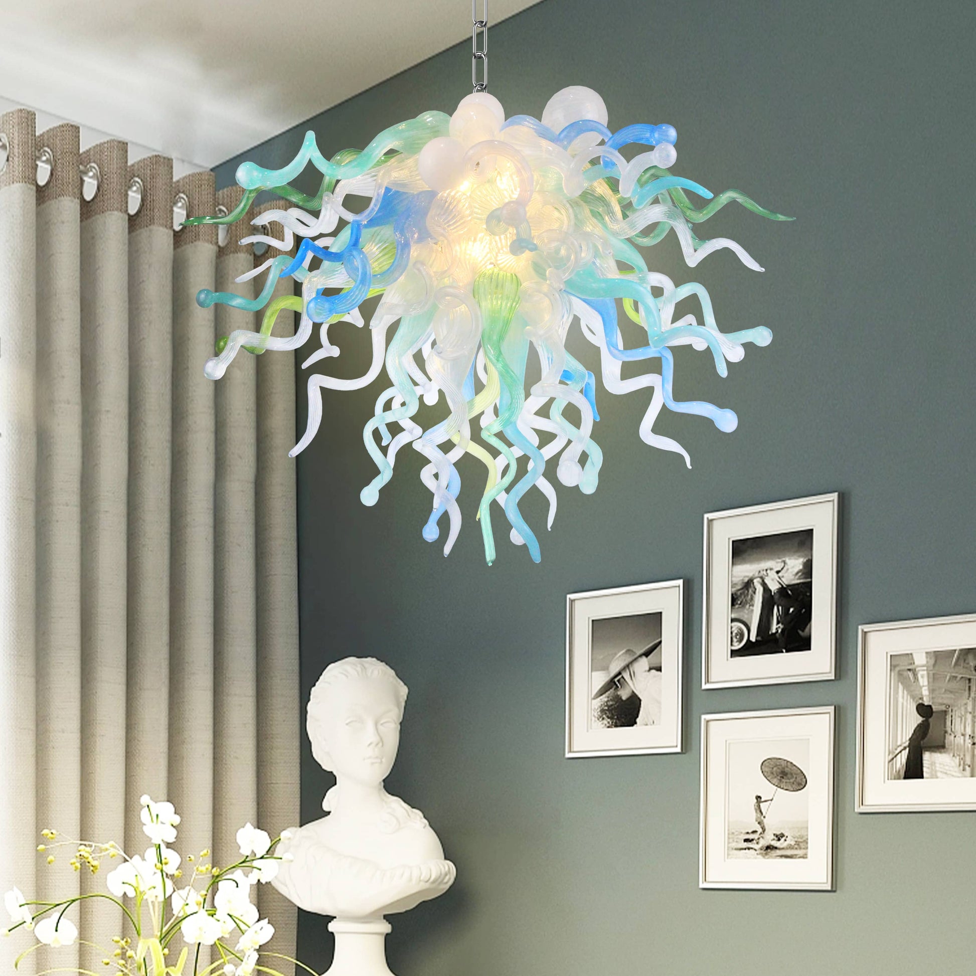 Chihuly Colorful chandelier hanging in a room with a gray wall, white curtains, and framed pictures.