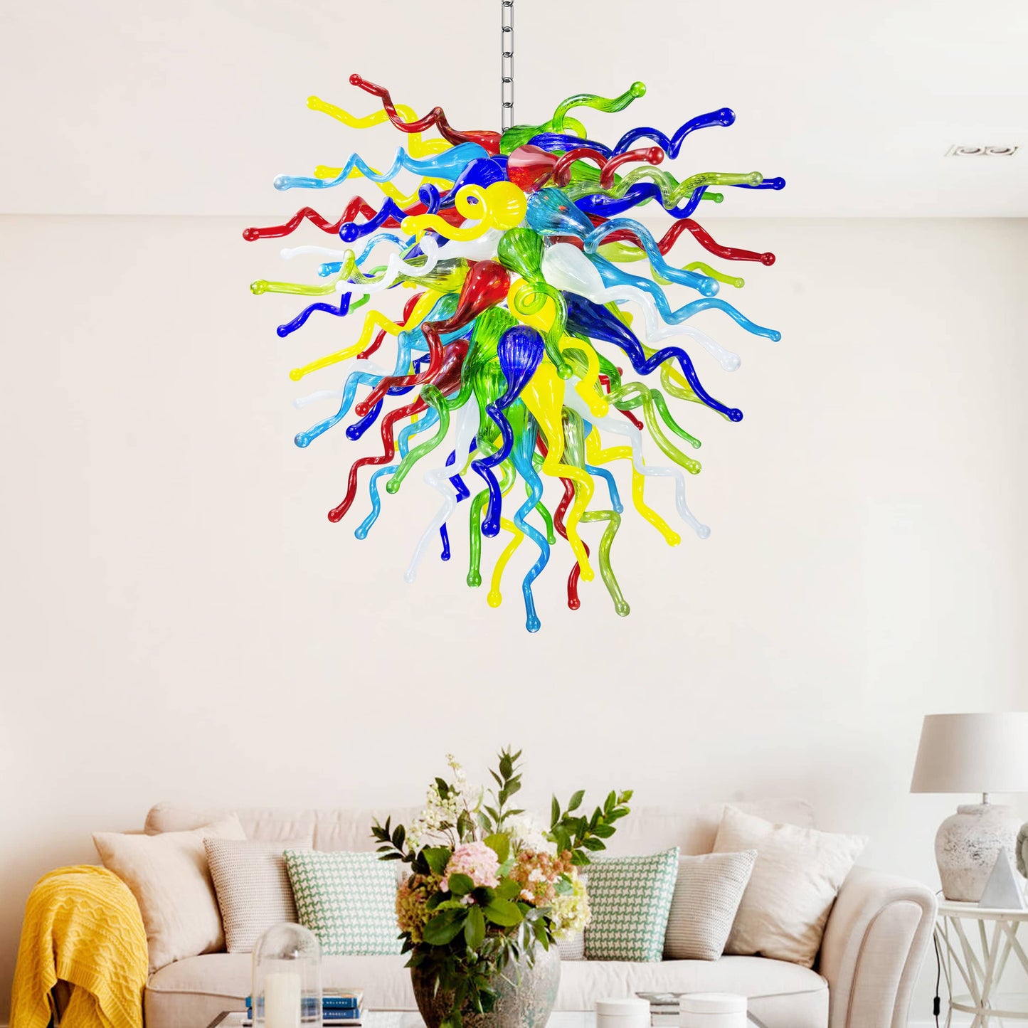 Multi-color hand blown glass chandelier illuminating a chic, cozy living space with a comfortable sofa and white walls.
