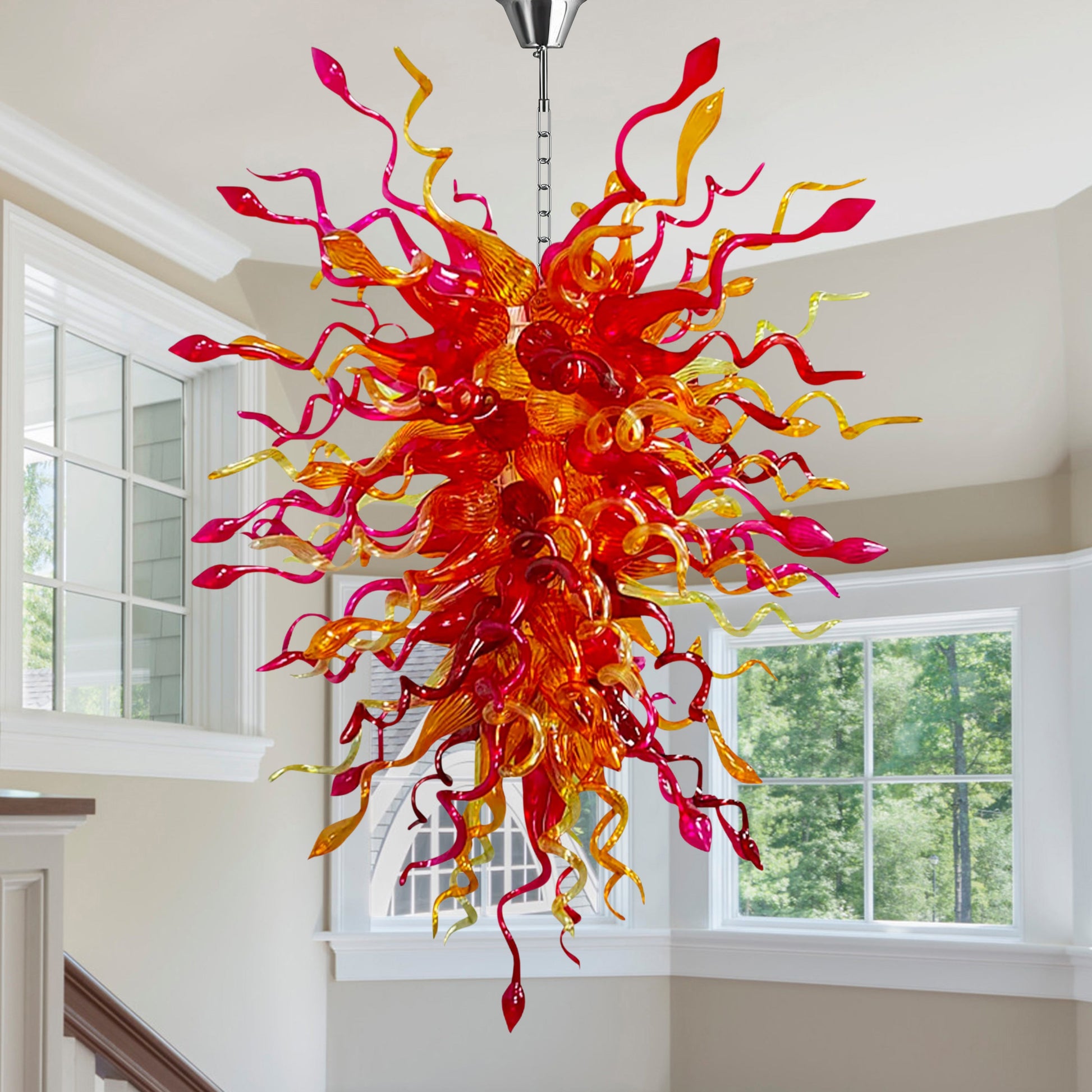 Brightly colored hand blown glass chandelier with red and yellow tones hanging above a modern staircase.
