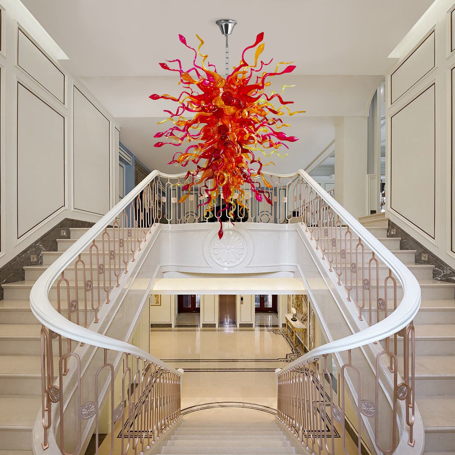 Large, colorful hand blown glass chandelier hanging over a grand, white marble staircase in a luxurious entryway.