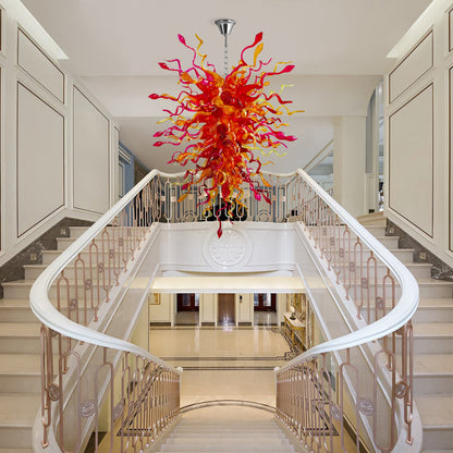Large, colorful hand blown glass chandelier hanging over a grand, white marble staircase in a luxurious entryway.