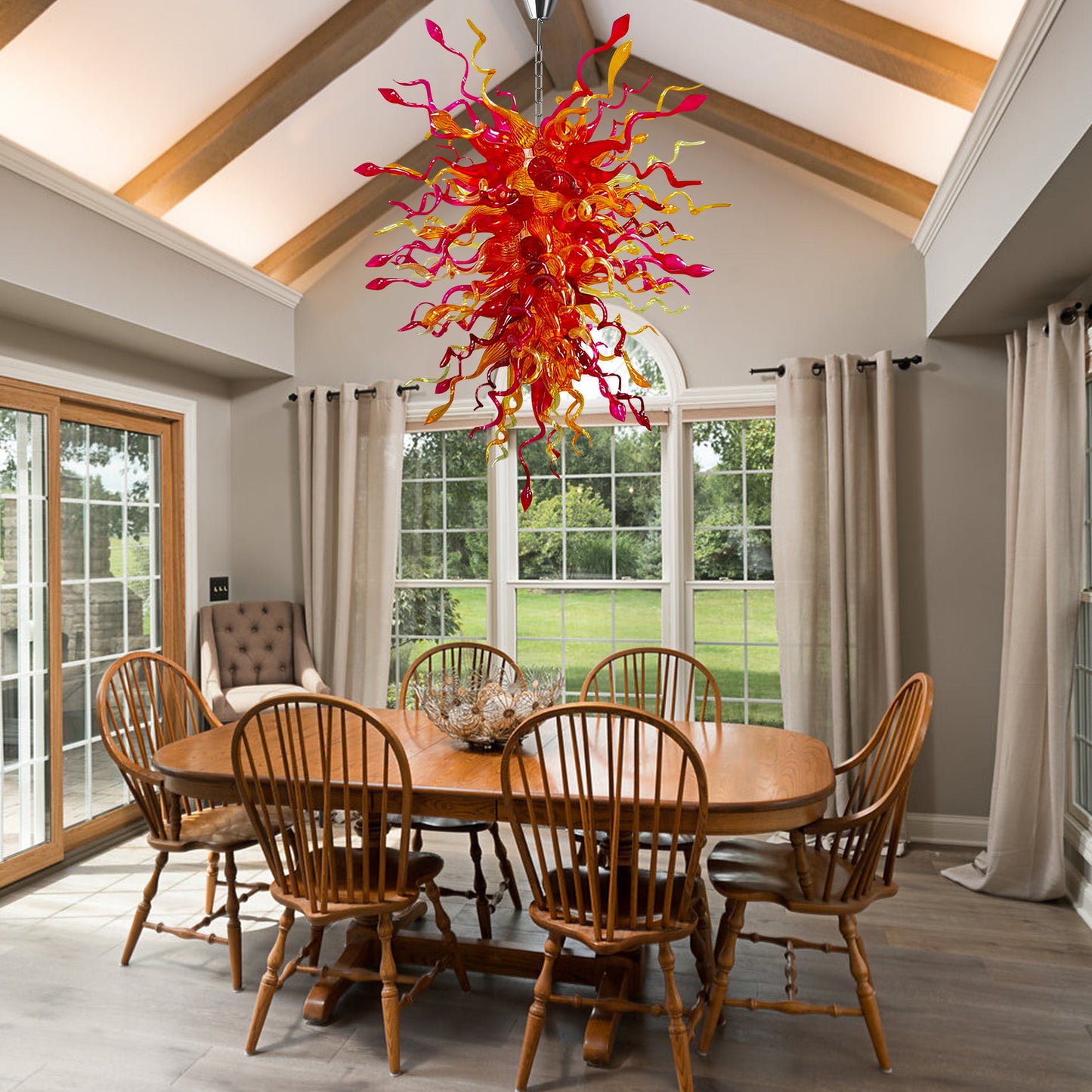 Red and yellow hand blown glass chandelier suspended above a wooden dining table.