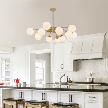 Adjustable gold 8-light frosted glass pendant bubble ball chandelier in white kitchen with black countertop.