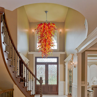 Custom size red and yellow hand blown glass chandelier centerpiece in a grand entryway/foyer with a curved staircase and high arched ceiling.