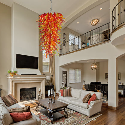 Long, custom hand blown glass chandelier in a two-story transitional living room with a fireplace and upper-level balcony.