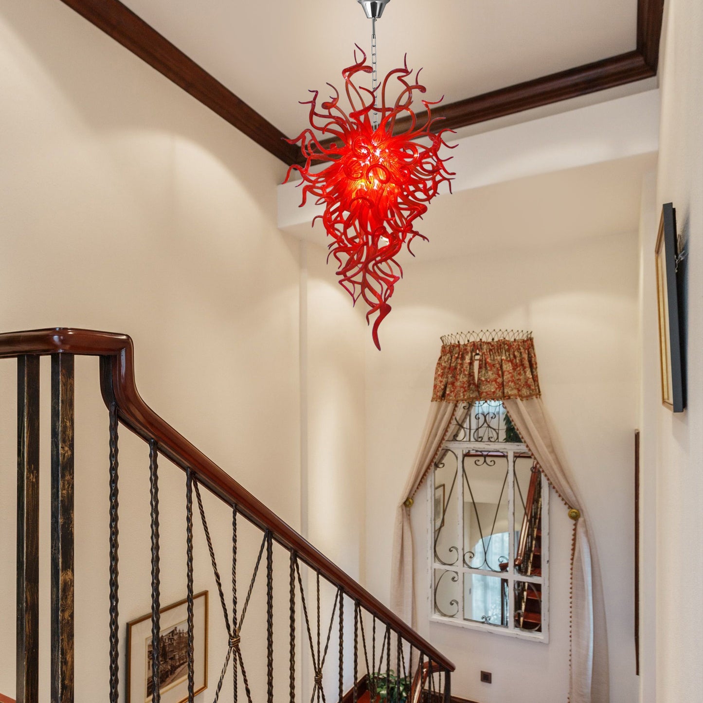 Red hand blown glass chandelier illuminating a transitional upper hallway near a window with decorative curtains.