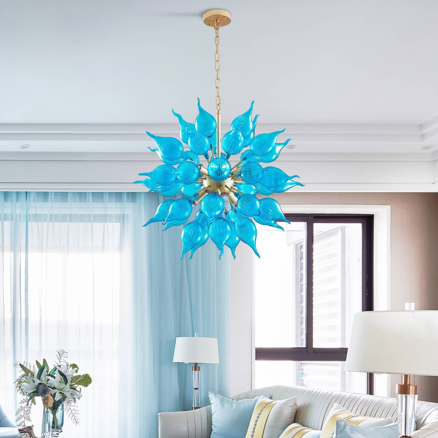 Turquoise blown glass chandelier in sputnik shape hanging in a living room with light blue curtains and a white sofa.
