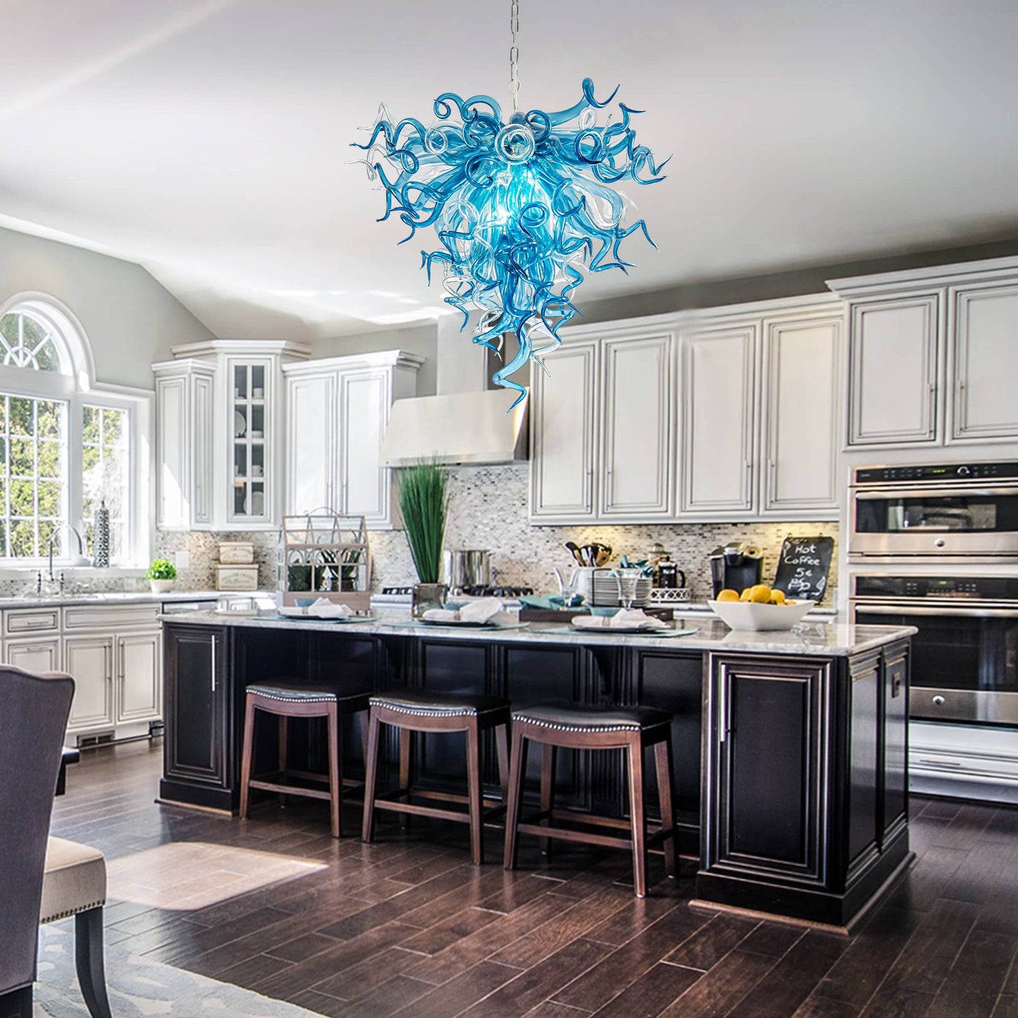 Modern kitchen with a blue chandelier, black island, and white cabinets.