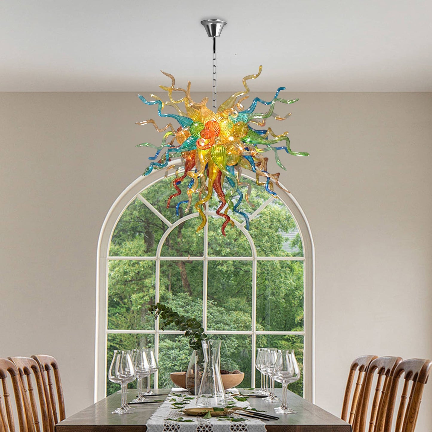 Chihuly glass chandelier hanging above a dining table with chairs in a room with large windows.