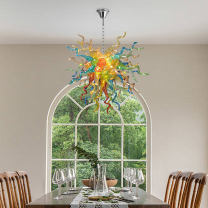 Chihuly glass chandelier hanging above a dining table with chairs in a room with large windows.