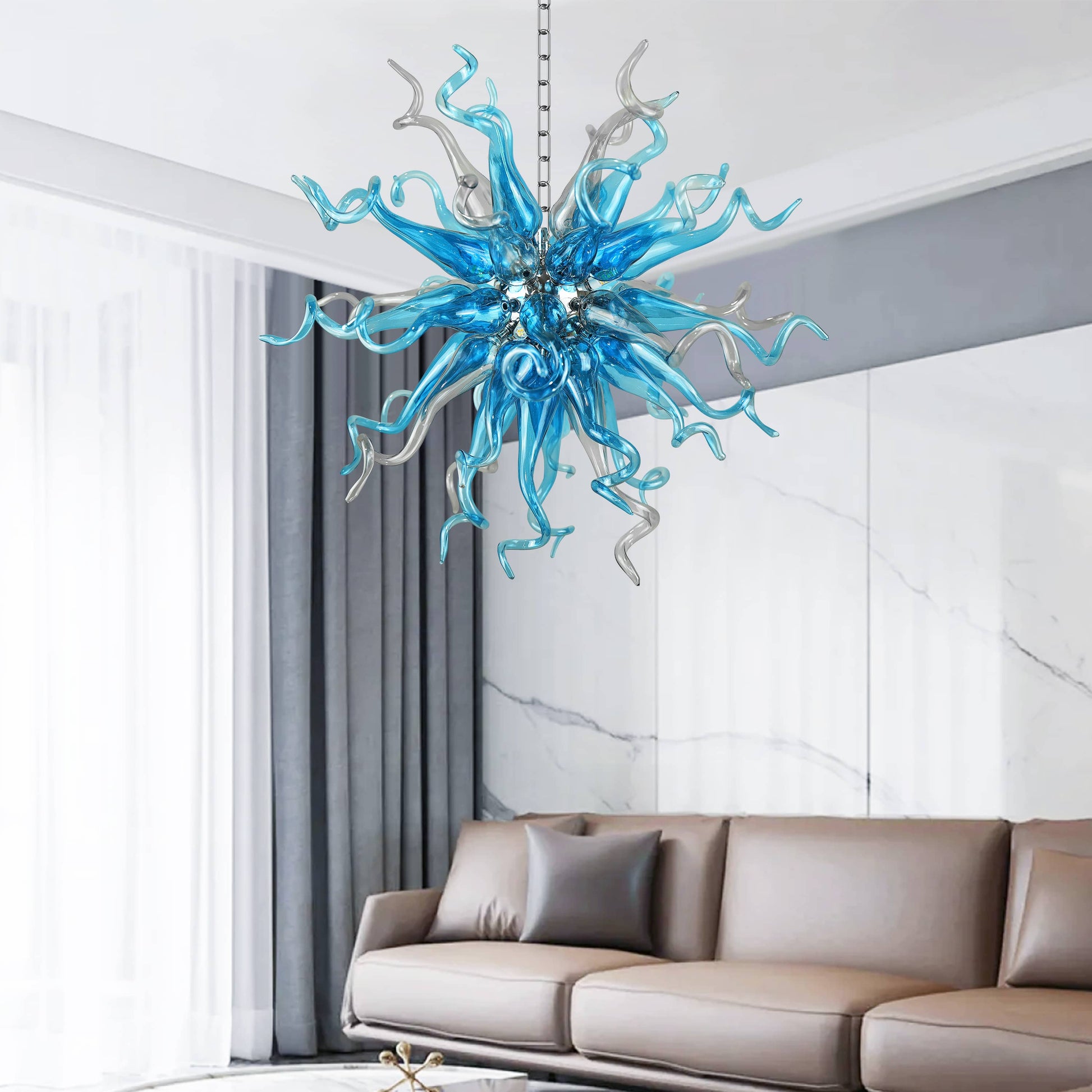 Blue blown glass chandelier hanging above a modern living room with a sofa and marble wall.