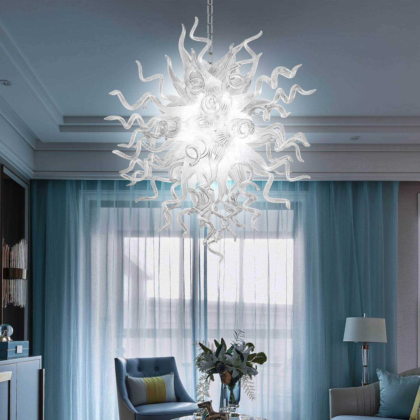 Chihuly style chandelier hanging in a living room with blue curtains and a gray sofa.