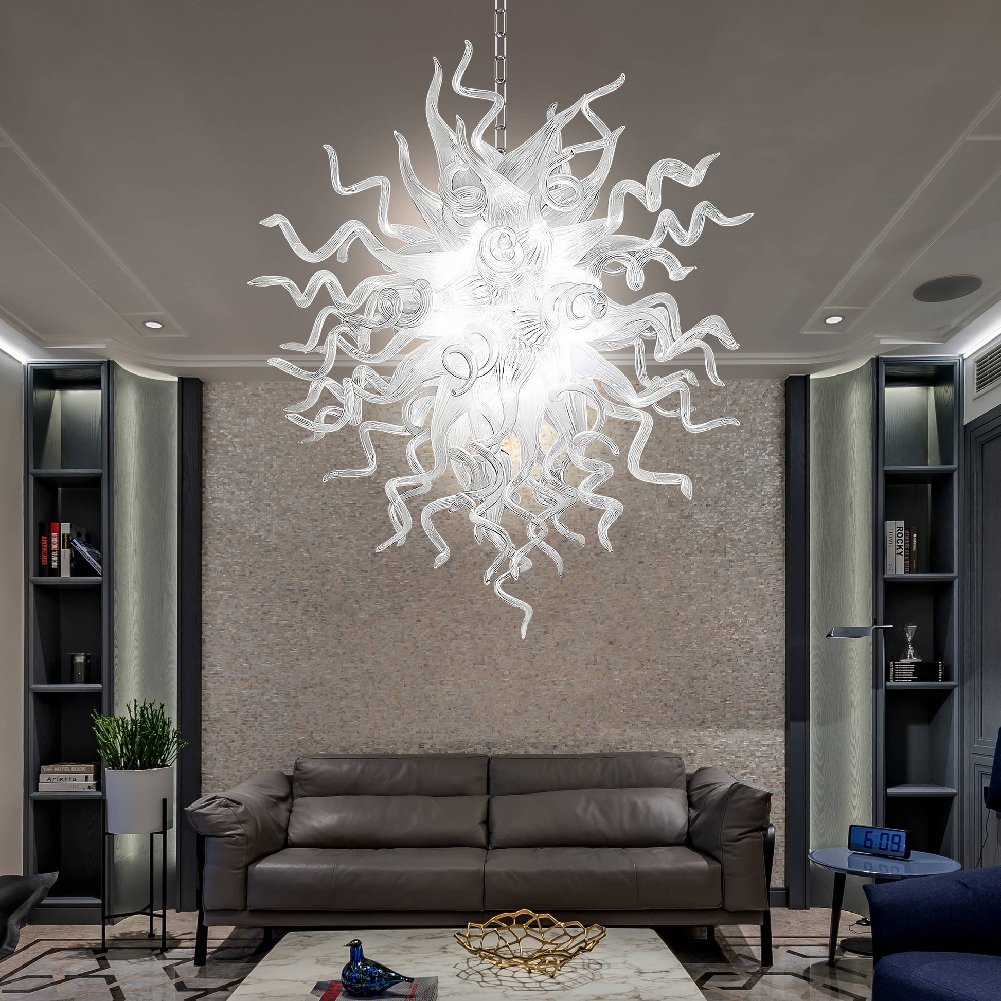 Chihuly style blown glass chandelier hanging in a living room with a brown sofa and bookshelves.